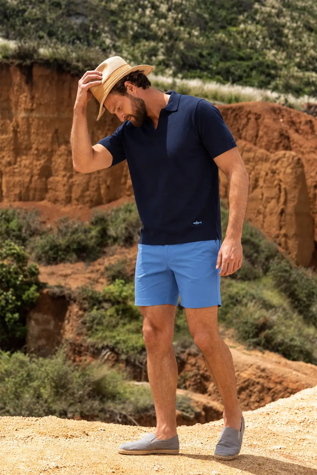 Hombre con pantaloneta azul medio, polo de punto azul oscuro, sombrero de palma iraca y alpargatas en un entorno de vegetación tropical